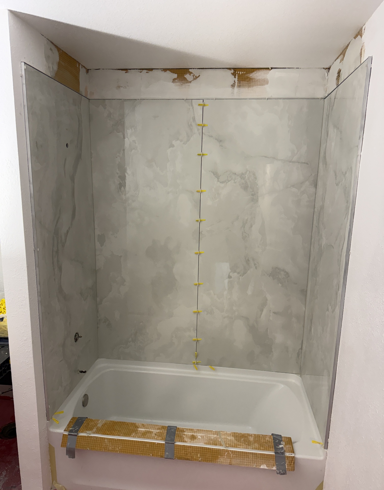 Bathtub surround being tiled with large veiny marble-look porcelain slabs and a recessed shower niche