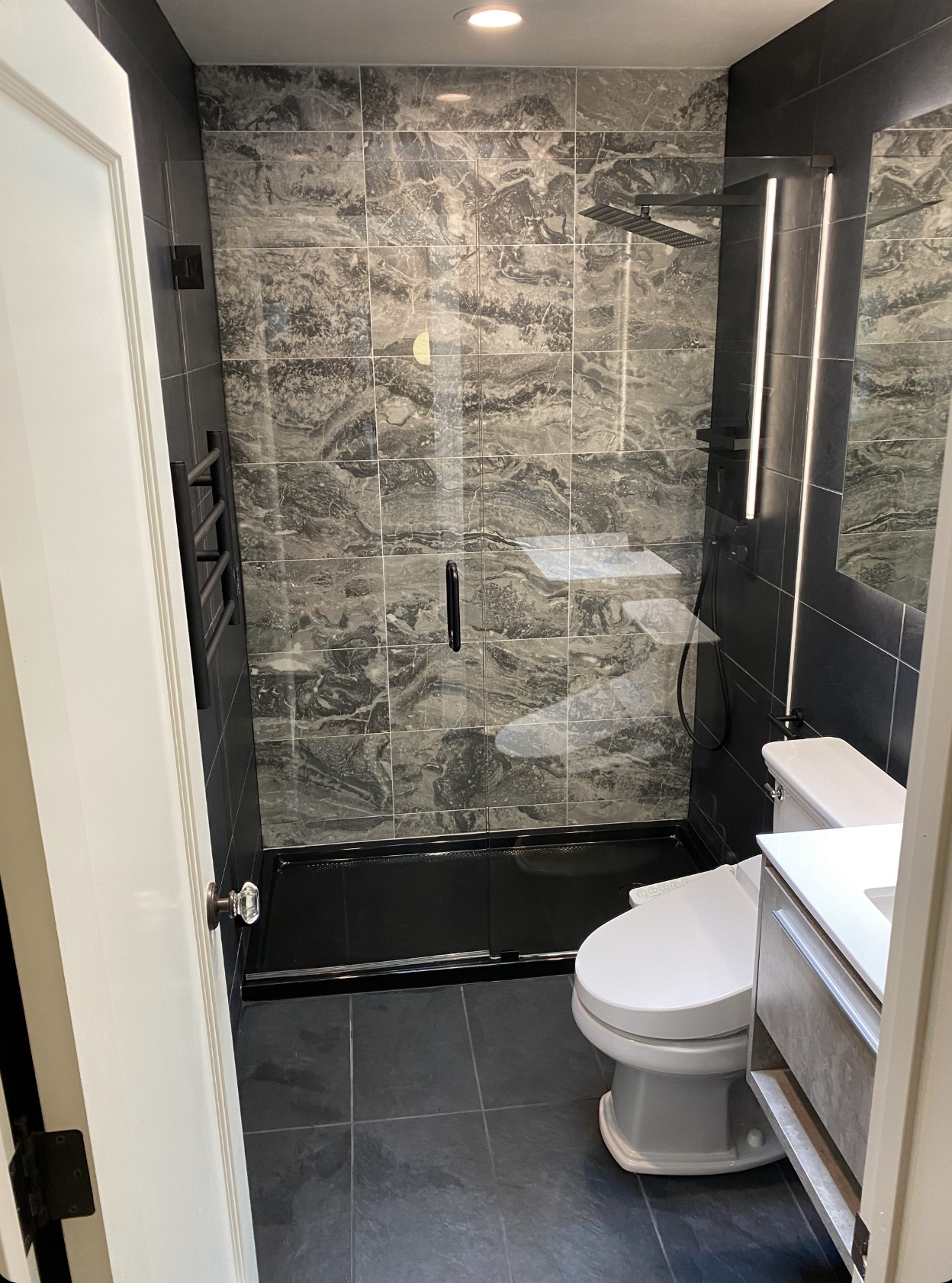 Finished black-and-gray marble-look bathroom with frameless glass shower and floating vanity