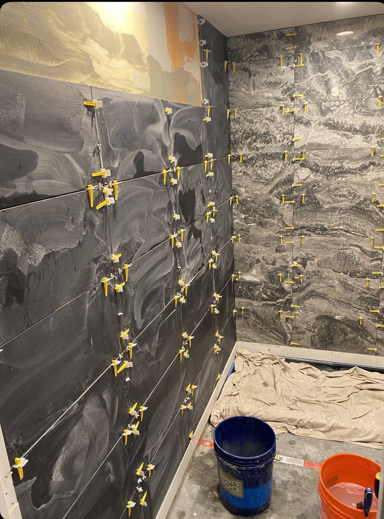 Dark marble-look porcelain tile shower during installation with leveling clips
