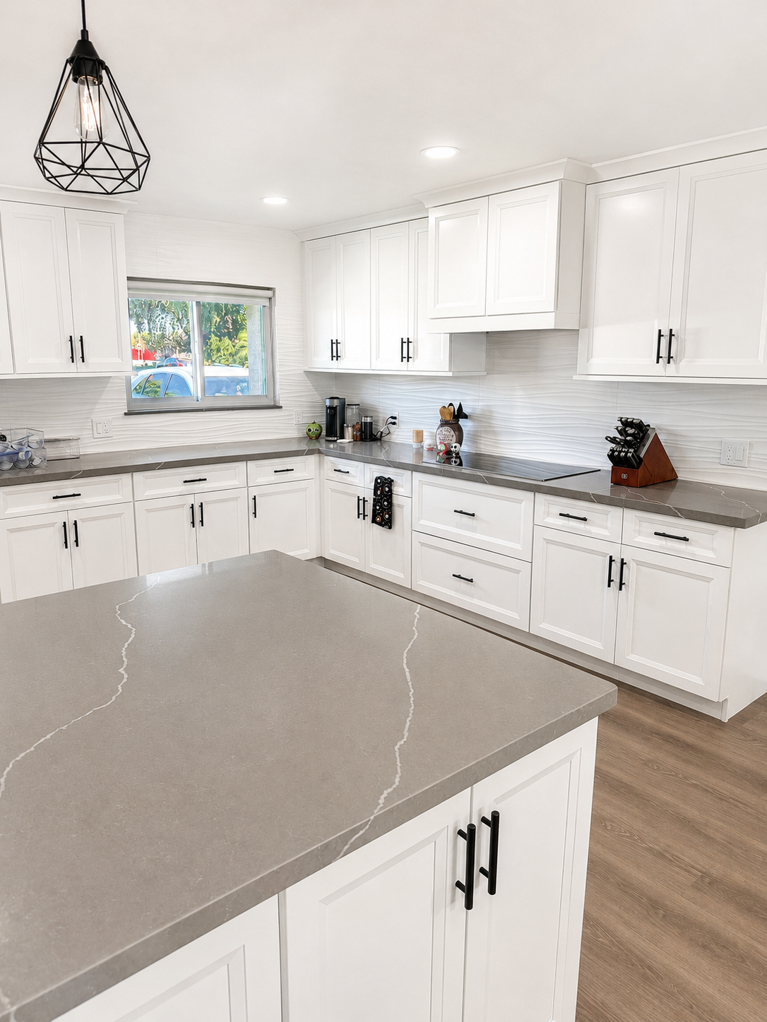 Bright, well-lit white shaker kitchen with gray quartz island, wave backsplash, and geometric pendant lighting