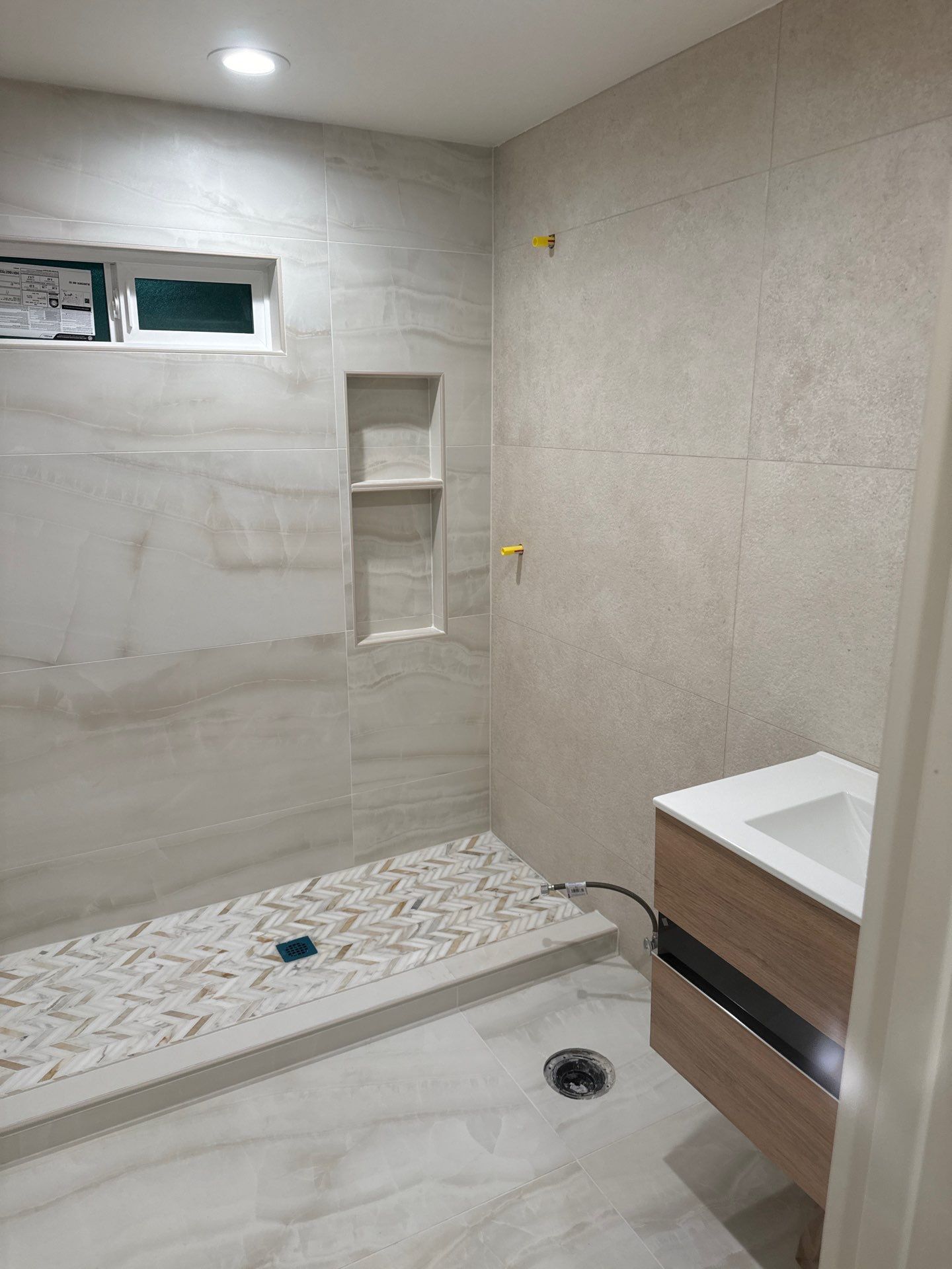 Beige large-format porcelain shower with herringbone marble floor during installation